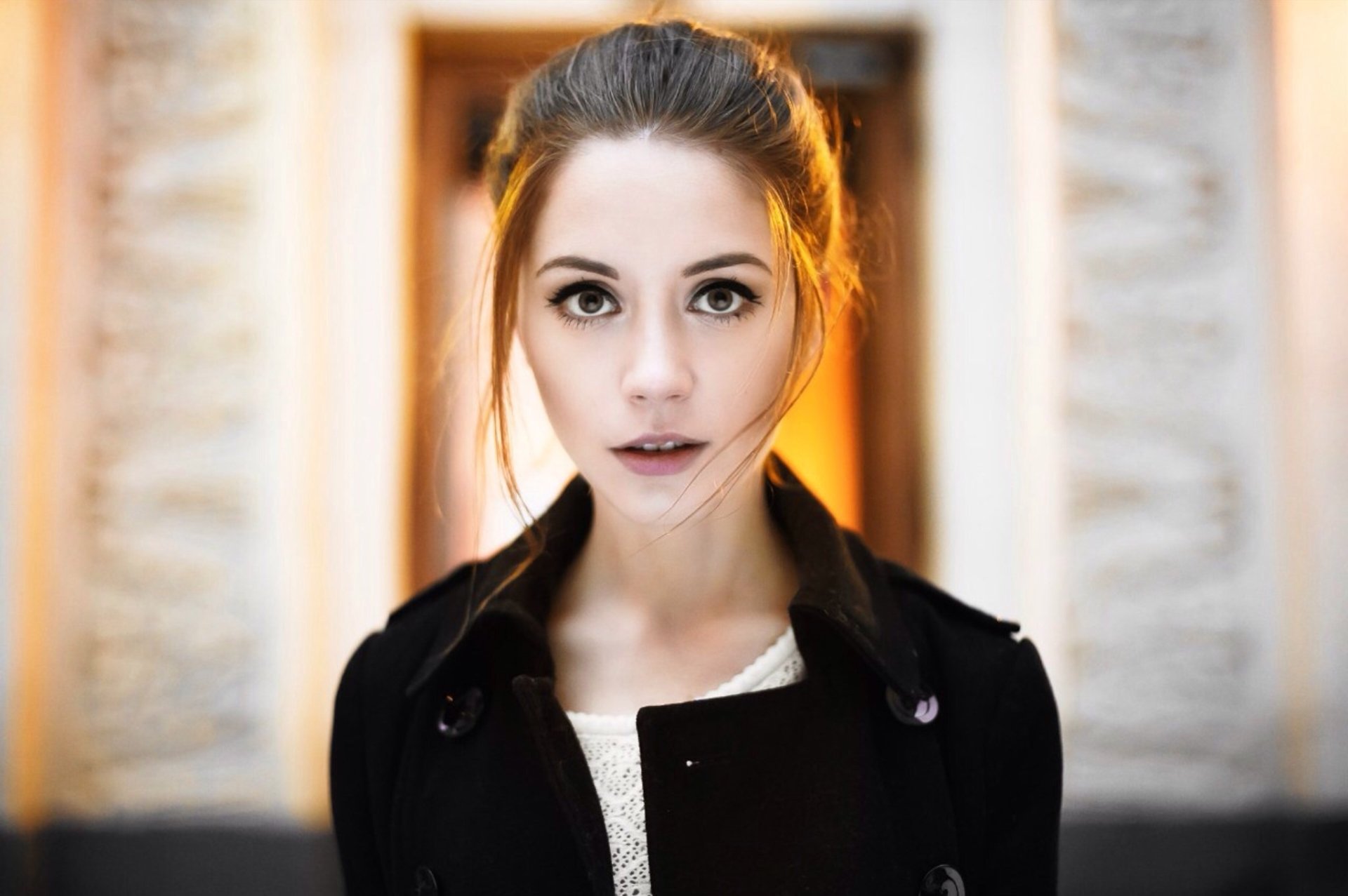 HD desktop wallpaper featuring a brunette woman model with brown eyes, softly lit against a blurred ornate background.