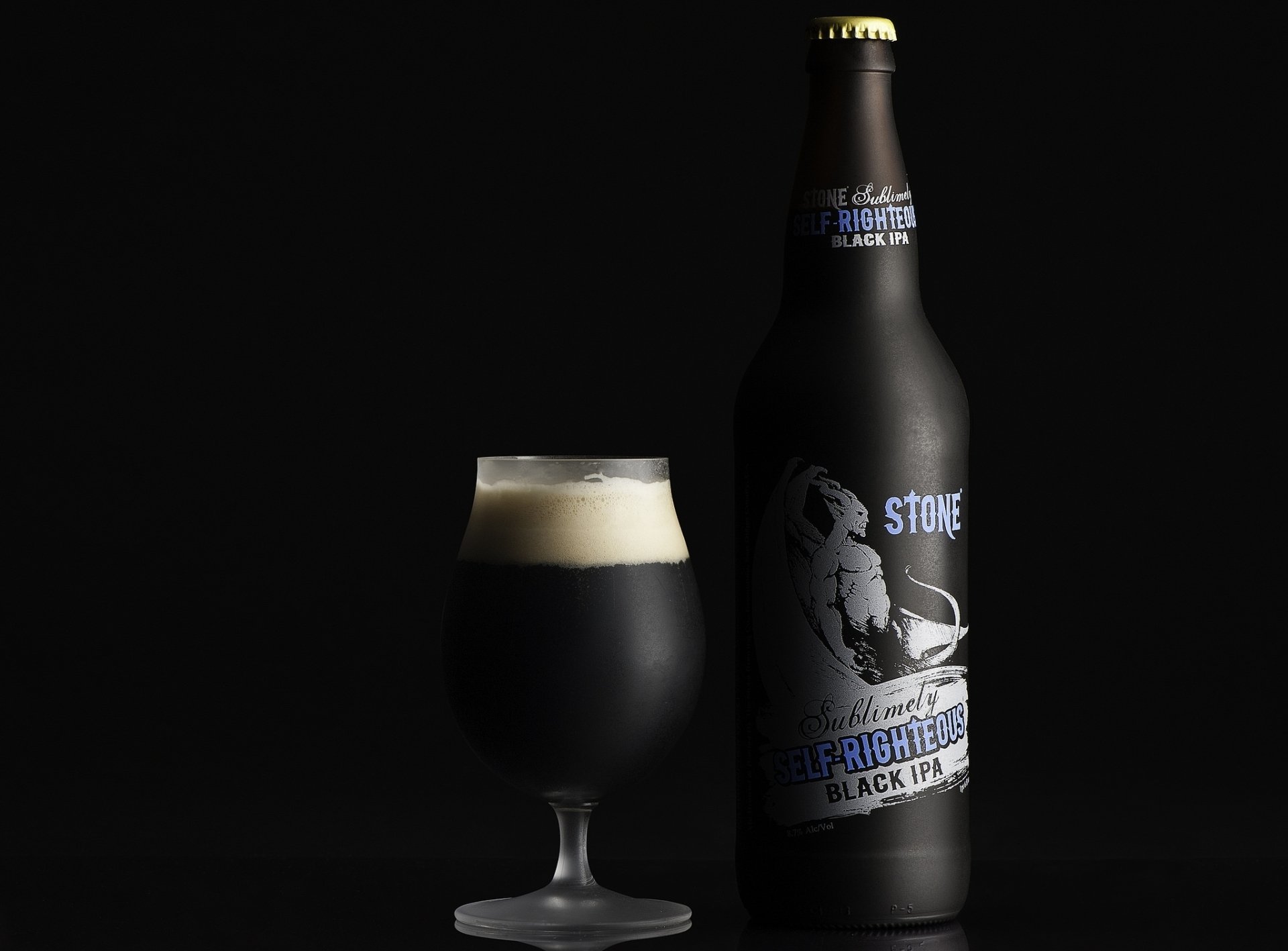 HD desktop wallpaper featuring a glass of dark beer with foam beside a black Stone Brewing bottle against a black background.