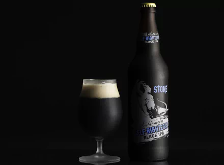 HD desktop wallpaper featuring a glass of dark beer with foam beside a black Stone Brewing bottle against a black background.