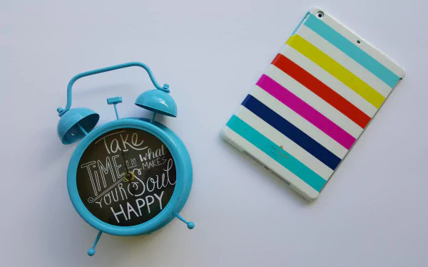 A vibrant blue alarm clock with an inspirational quote next to a colorful striped tablet, creating a motivational desktop wallpaper in 4K Ultra HD.