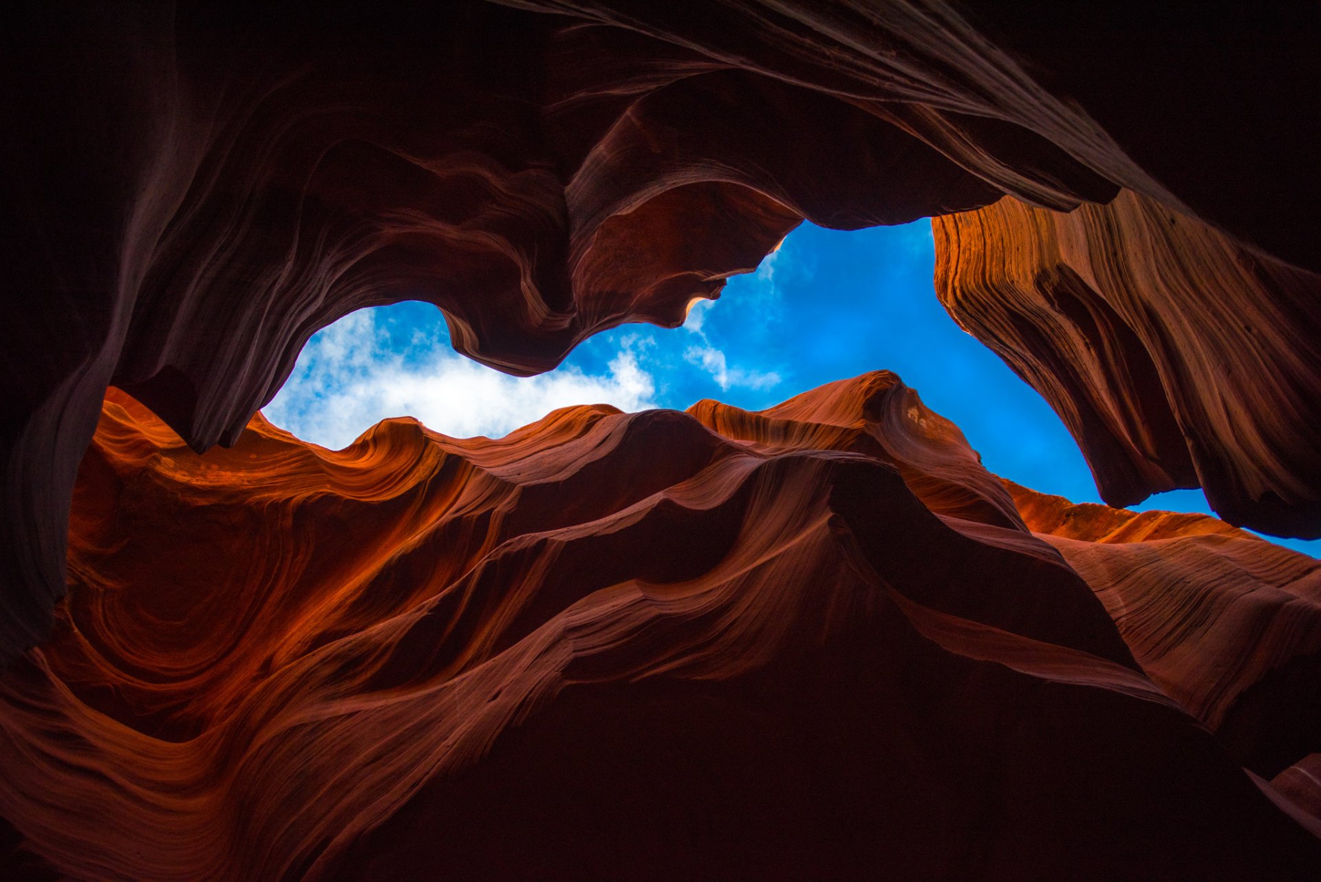 HD PC desktop wallpaper: Antelope Canyon, Arizona — sunlit red sandstone waves and layered canyon walls framing a vivid blue sky, showcasing nature’s sculpted textures.