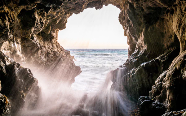 View from inside a rocky cave looking out at the ocean horizon, with waves crashing and mist rising, captured in stunning 8K Ultra HD quality.