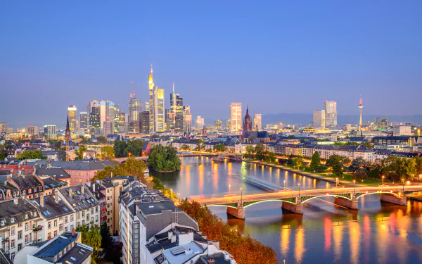 A stunning evening view of Frankfurt, showcasing skyscrapers illuminated along the river, with bridges reflecting the vibrant city lights in this picturesque German landscape.