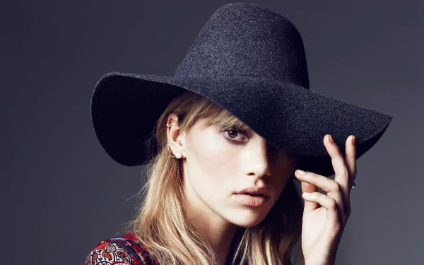 Close-up HD wallpaper of English model and celebrity Suki Waterhouse with blonde hair, brown eyes, and a large black hat partially shading her face.
