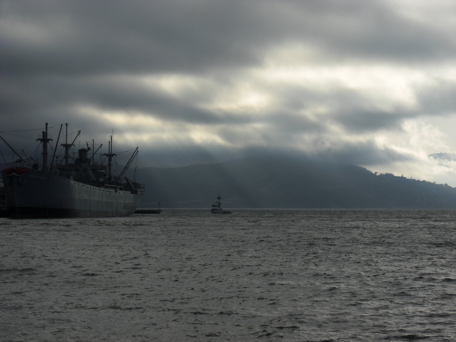 A dramatic HD wallpaper featuring a large ship on moody waters, with a smaller vessel navigating nearby under a cloudy sky, creating a striking maritime scene.