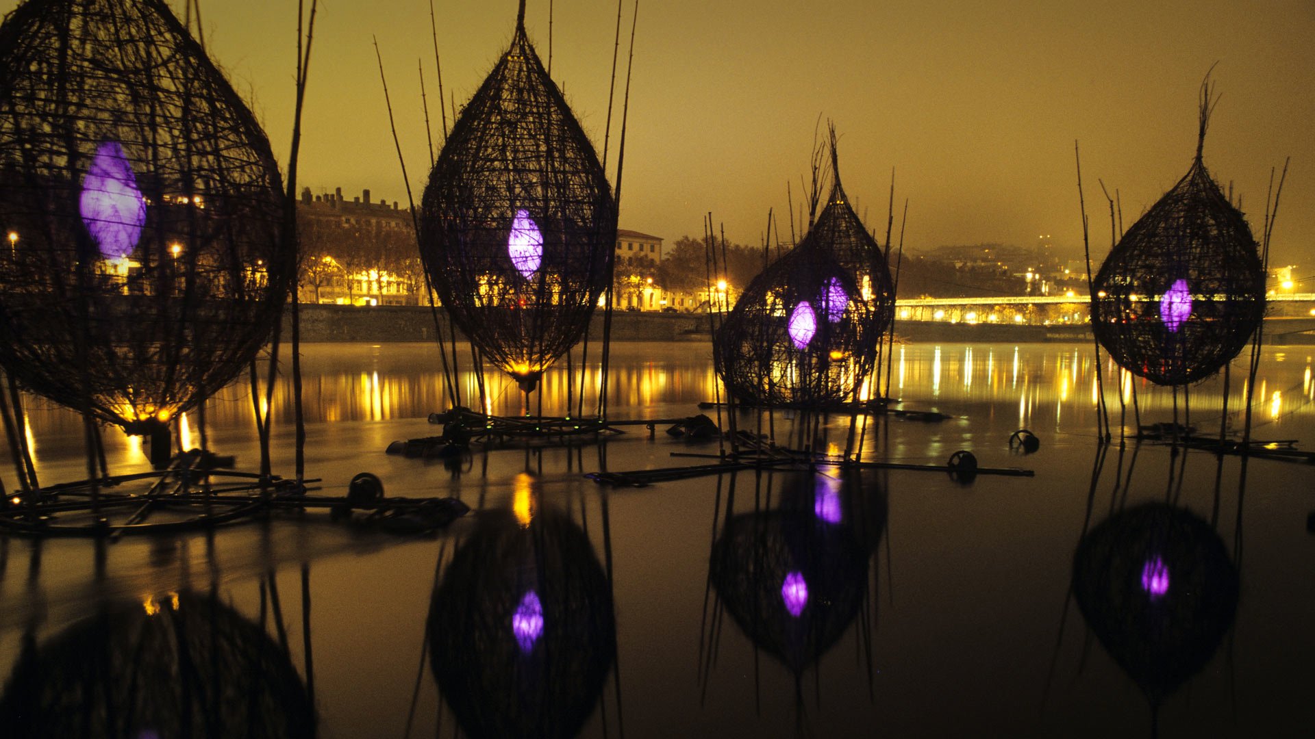 A serene night scene of the River Lyon in France, featuring illuminated reflections from artistic structures on the water, creating a stunning photographic backdrop.