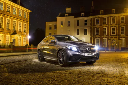 A silver Mercedes-Benz GL-Class SUV parked on a cobblestone street at night, illuminated by warm streetlights in a cityscape, captured in 4K Ultra HD.