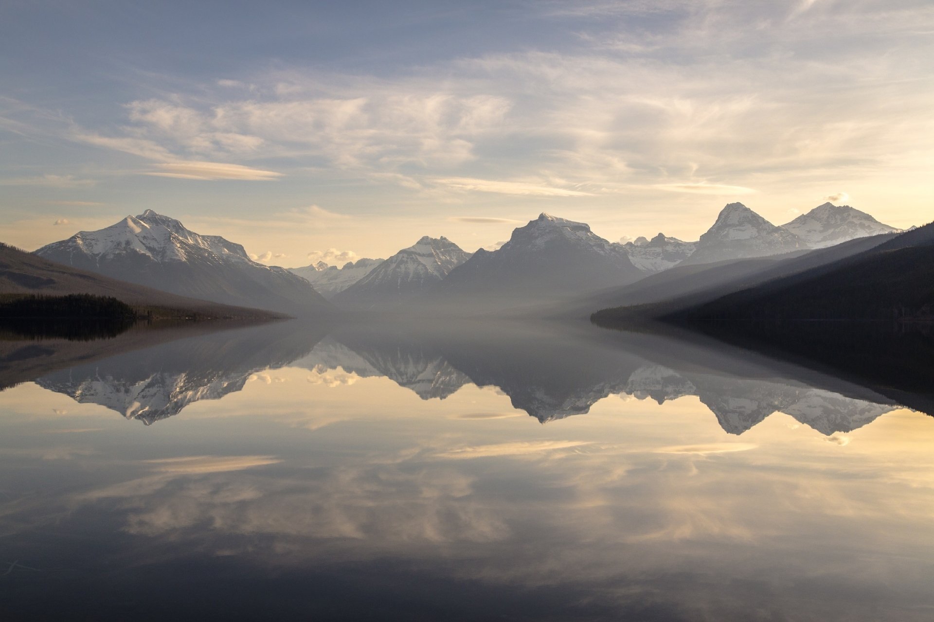 Scenic view of Montana's Glacier National Park with mountain peaks reflecting in the calm waters of Lake McDonald, showcasing wilderness and nature in HD quality.
