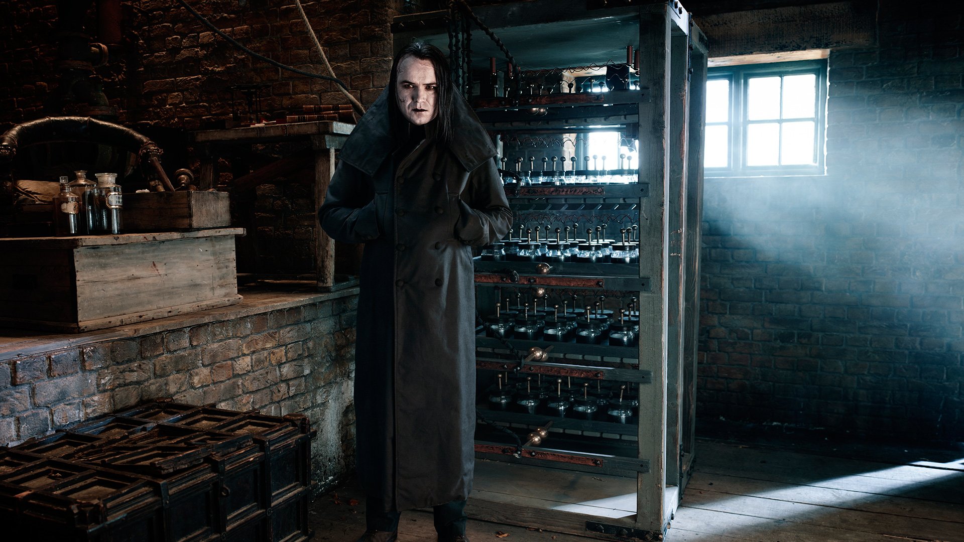 HD PC desktop wallpaper/background from the TV show Penny Dreadful: a pale, cloaked figure stands in a dim, brick-walled cellar, window light cutting through dust onto racks of jars and equipment.
