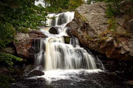 A scenic waterfall cascading over rocks surrounded by lush greenery in Connecticut, USA, captured as a high-definition nature wallpaper.