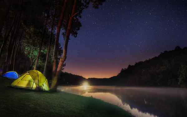 A tranquil camping scene features illuminated tents beside a serene lake, framed by a lush forest under a starry night sky, creating a captivating 4K Ultra HD desktop wallpaper.