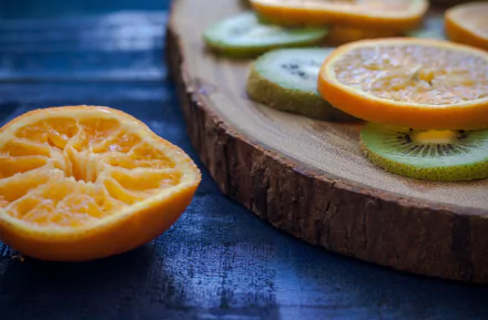 HD desktop wallpaper featuring close-up of sliced orange and kiwi fruit arranged on a wooden surface with a dark blue textured background.