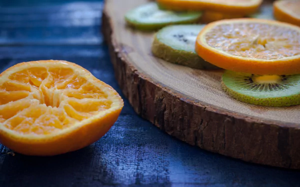 HD desktop wallpaper featuring close-up of sliced orange and kiwi fruit arranged on a wooden surface with a dark blue textured background.