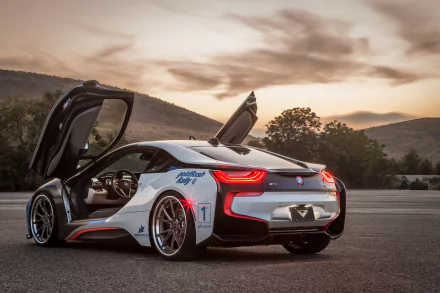 A striking BMW i8 supercar in white, featuring distinctive upward-opening doors, parked against a scenic backdrop at sunset. This HD image showcases the vehicle's sleek design.