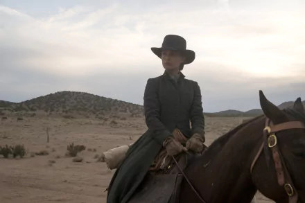 4K Ultra HD desktop wallpaper: woman in a dark coat and wide-brim hat on horseback crossing a desert, cinematic scene from the film Jane Got a Gun.
