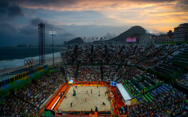 A vibrant beach volleyball scene during sunset, showcasing an energetic crowd at a sporting event. This HD image captures the excitement of volleyball in a stunning outdoor setting.