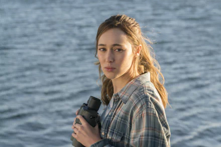 Alycia Debnam-Carey as Alicia Clark from Fear the Walking Dead stands by the water, holding binoculars, in this stunning 8K Ultra HD wallpaper.