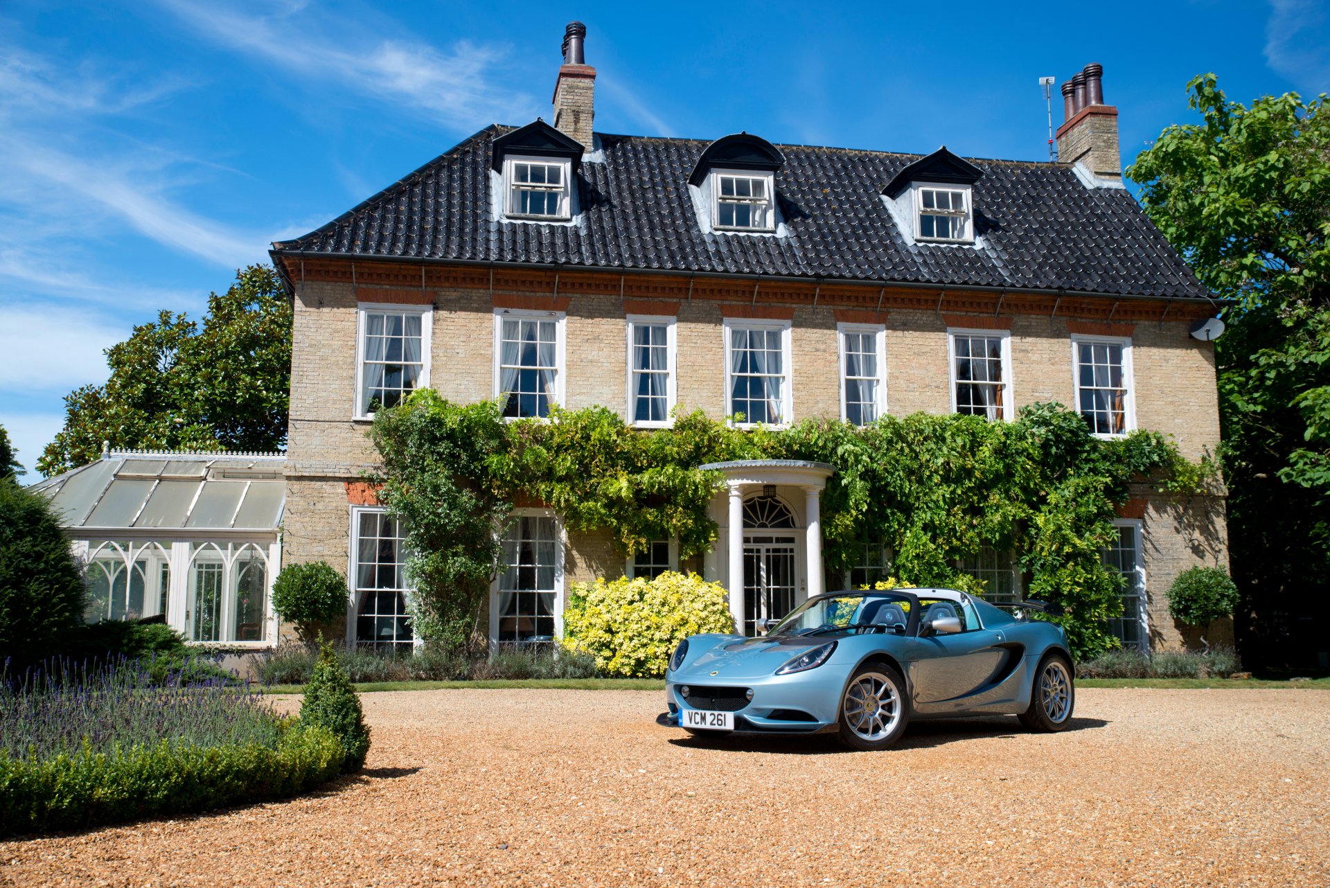 A sleek Lotus Elise supercar parked in front of a classic countryside house, captured in stunning 4K Ultra HD as a vibrant PC desktop wallpaper.