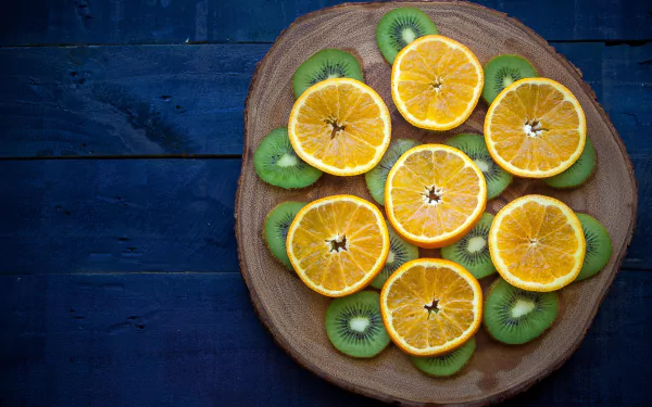 HD desktop wallpaper featuring a wooden plate with sliced orange fruits and kiwi arranged on a dark blue wooden background.