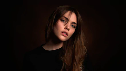 A brunette woman with striking blue eyes gazes confidently at the camera, captured in a high-definition desktop wallpaper against a dark background.