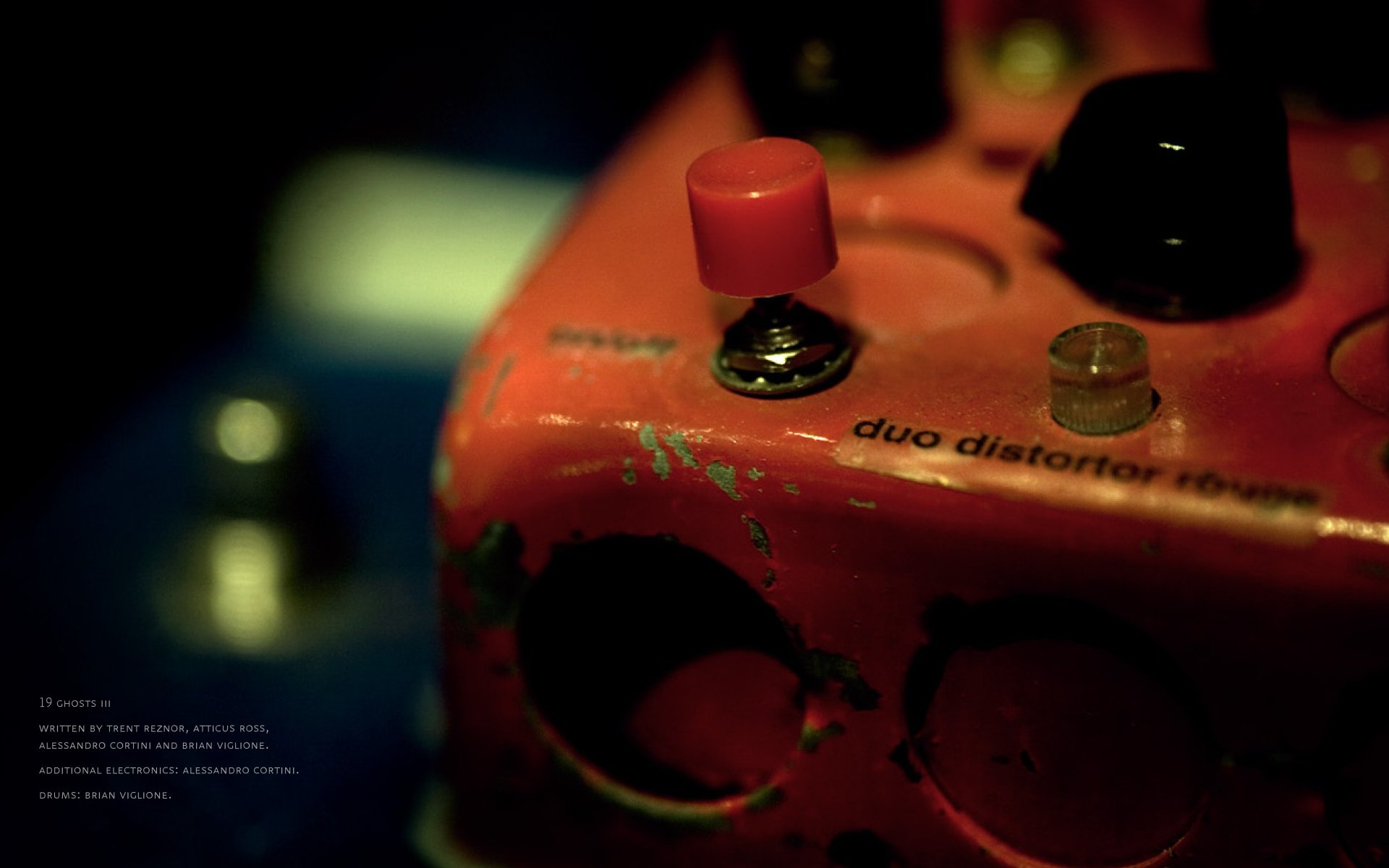 Close-up of a red guitar effects pedal labeled duo distorter on a dark background, featured as a HD PC desktop wallpaper inspired by Nine Inch Nails music.