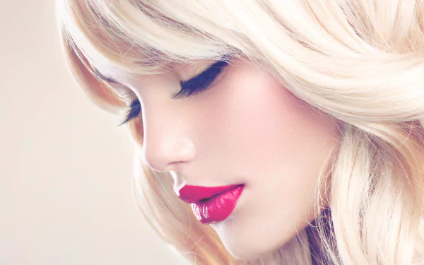 A close-up of a blonde woman with striking red lipstick framed by flowing hair, set against a soft, light background, creating an elegant HD desktop wallpaper.