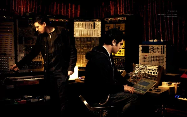 HD PC desktop wallpaper featuring Nine Inch Nails members working with vintage synthesizers and audio equipment in a dimly lit studio, capturing a music production vibe.