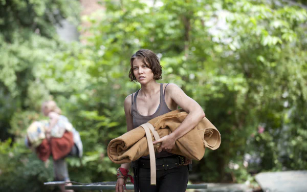 Lauren Cohan from The Walking Dead carries a rolled mat through a lush, green outdoor setting in this HD PC desktop wallpaper and background.