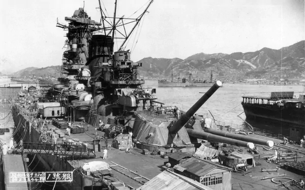 HD wallpaper of the Japanese battleship Yamato, a military warship, docked with surrounding mountains and other ships in the background.