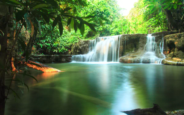 Sunlit tropical Thailand waterfall spilling into a serene creek amid lush jungle — tranquil 5K Ultra HD PC desktop wallpaper/background.