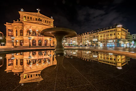 Night view of Frankfurt's illuminated opera house and surrounding city buildings reflected in a fountain pool, showcasing the man-made architectural beauty of Germany.