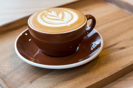 A beautifully crafted latte in a brown cup, featuring intricate latte art, rests on a wooden tray. This image serves as a 4K Ultra HD desktop wallpaper showcasing coffee culture.