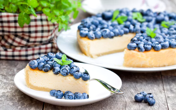 A slice of blueberry pie topped with fresh blueberries and mint leaves on a white plate, with the remaining pie and a potted plant in the background, shown in 4K Ultra HD.