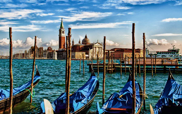 A vibrant HD desktop wallpaper of Venice, Italy, showcasing gondolas on a canal with historic city buildings and a bright blue sky in the background.