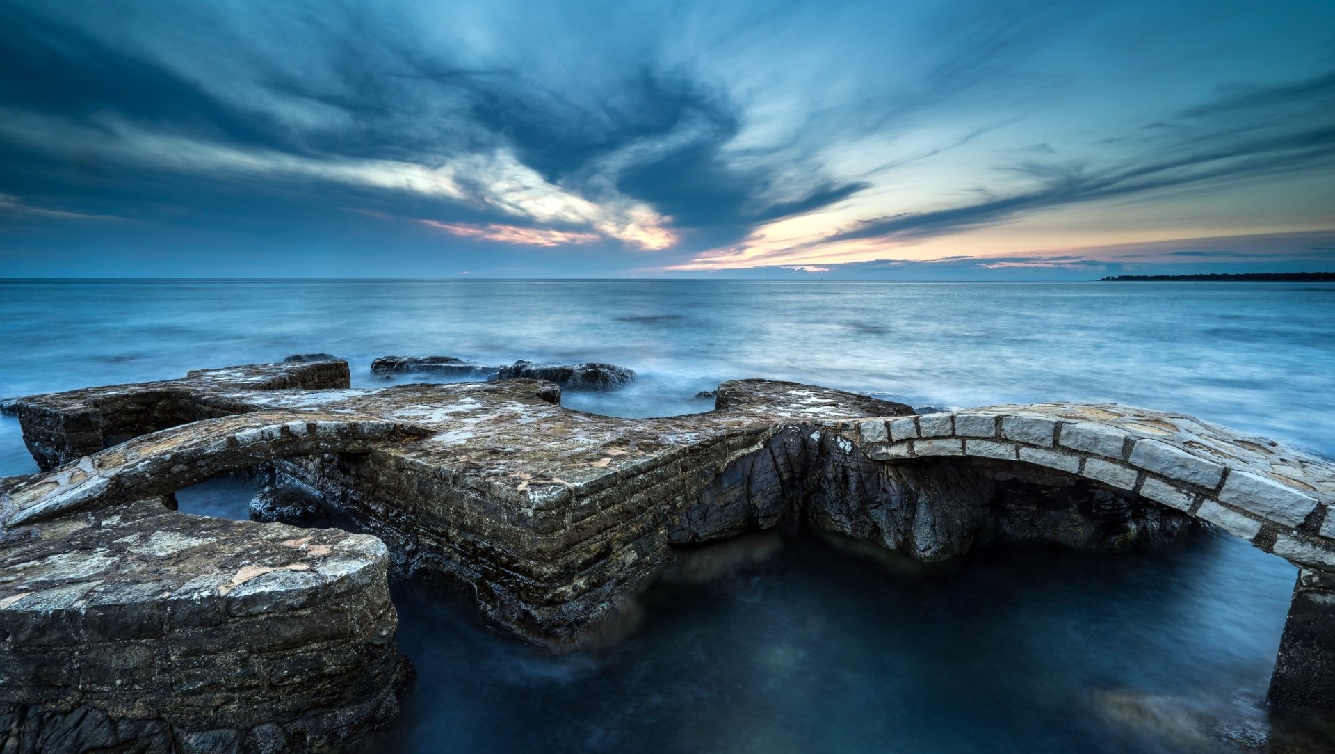 HD PC desktop wallpaper featuring a serene ocean view with rocky formations under a dramatic sky at the horizon.