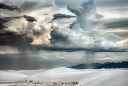HD desktop wallpaper of a dramatic desert landscape featuring white sand dunes beneath a vast sky filled with towering, textured clouds.