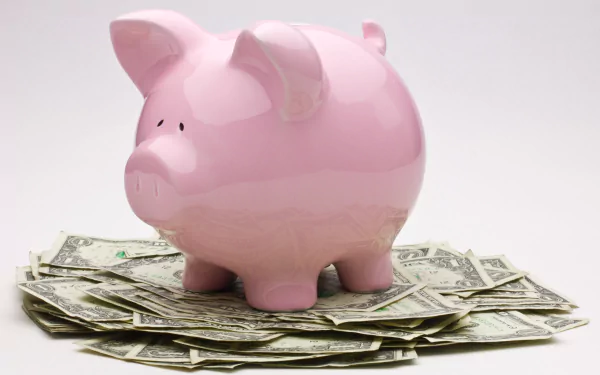Man-made pink piggy bank atop US dollar bills, money-themed 2K Quad HD PC desktop wallpaper/background.