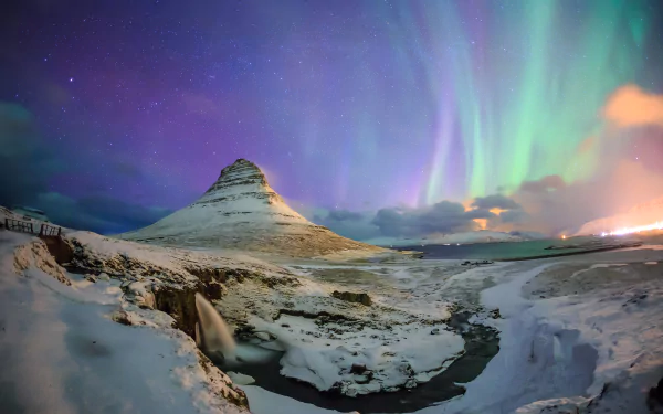 Aurora borealis lights the sky above snowy Kirkjufell mountain, Kirkjufoss waterfall, and a winding river in Iceland’s winter landscape.