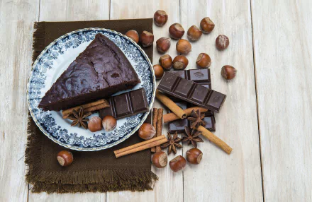HD desktop wallpaper featuring a still life of chocolate cake, hazelnuts, cinnamon sticks, and spices arranged on a wooden surface with a decorative plate.