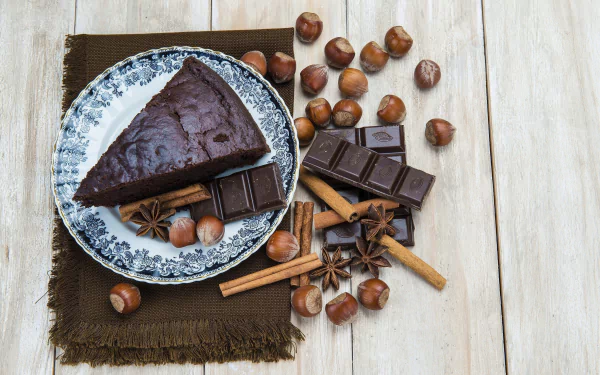 HD desktop wallpaper featuring a still life of chocolate cake, hazelnuts, cinnamon sticks, and spices arranged on a wooden surface with a decorative plate.