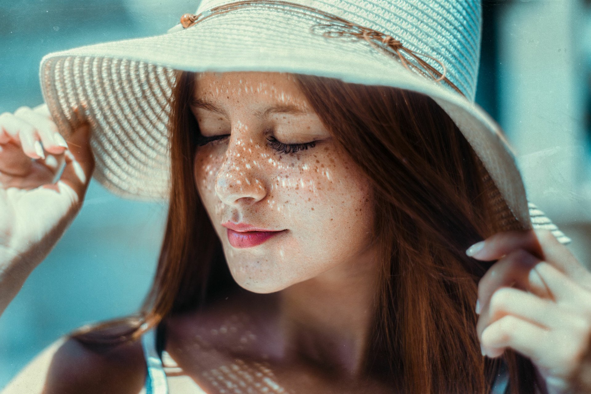 A close-up of a redhead woman with freckles, wearing a wide-brimmed hat, eyes closed, captured in soft daylight; HD desktop wallpaper and background.