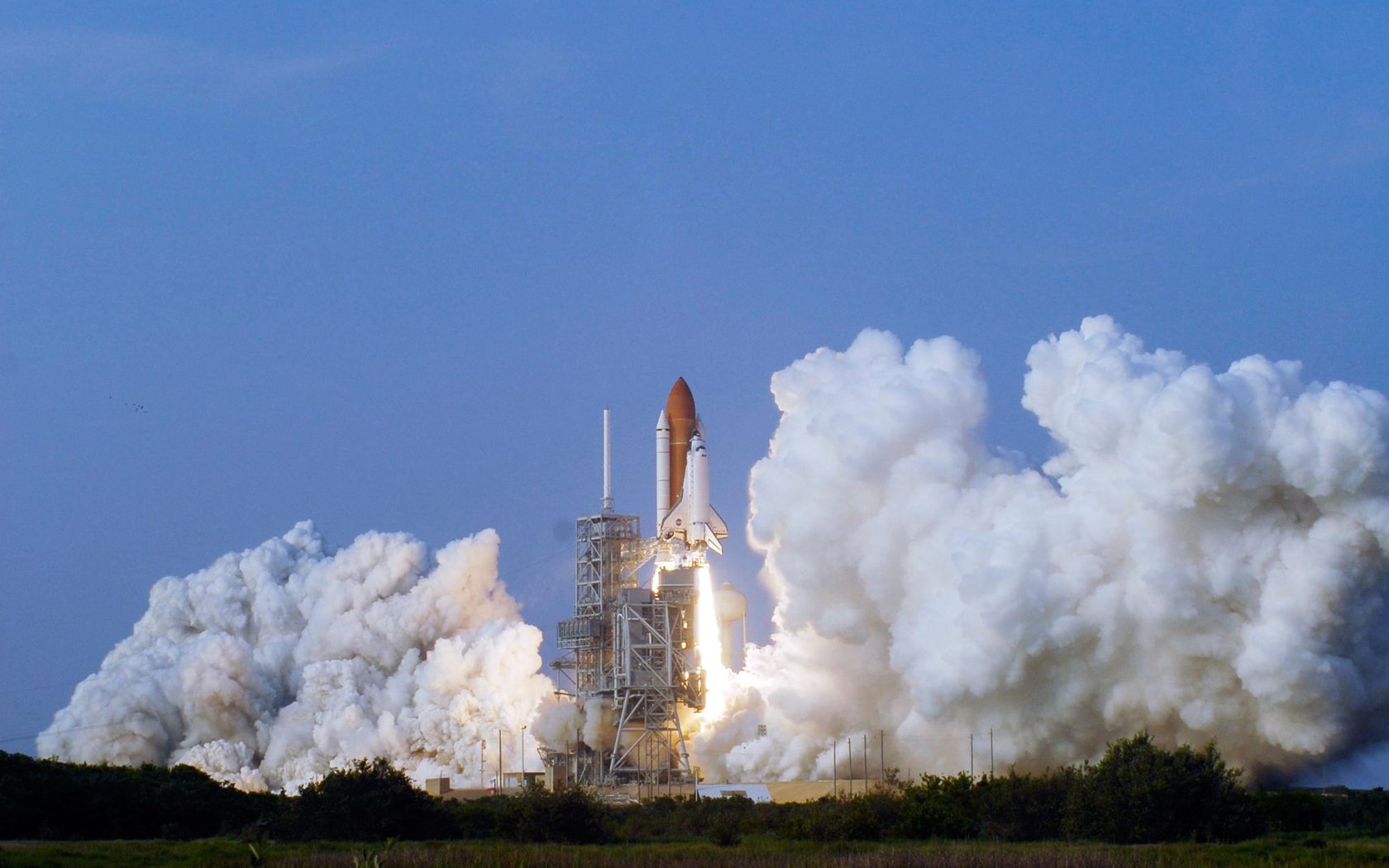 HD PC desktop wallpaper of a space shuttle vehicle launching, surrounded by billowing smoke against a clear blue sky.