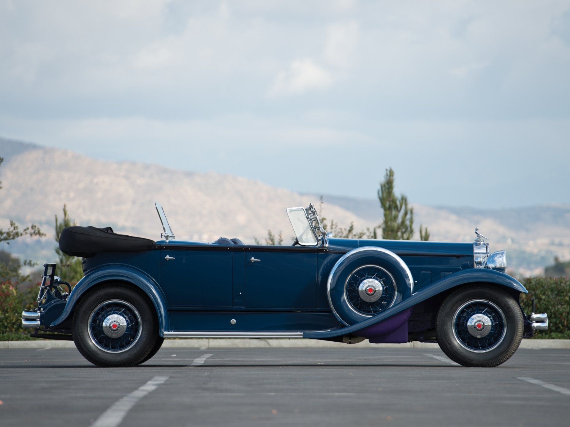 HD PC desktop wallpaper: side profile of a deep-blue 1931 Packard Deluxe Eight Sport Phaeton parked before a soft mountain backdrop, showcasing the vintage vehicle.