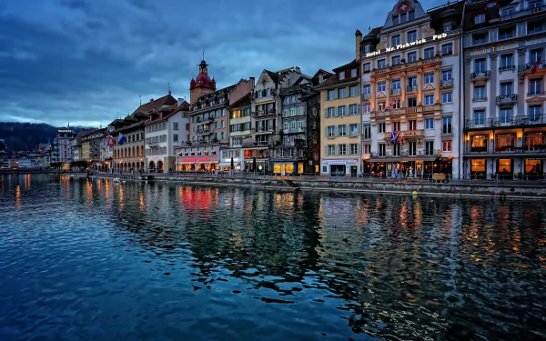 Panoramic view of man-made waterfront houses in Lucerne, Switzerland, reflecting off the calm water under a moody evening sky.