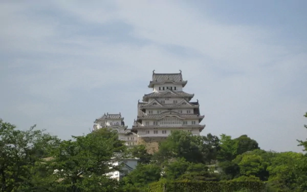 HD desktop wallpaper featuring the majestic man-made Himeji Castle standing prominently against a clear sky, surrounded by lush greenery.