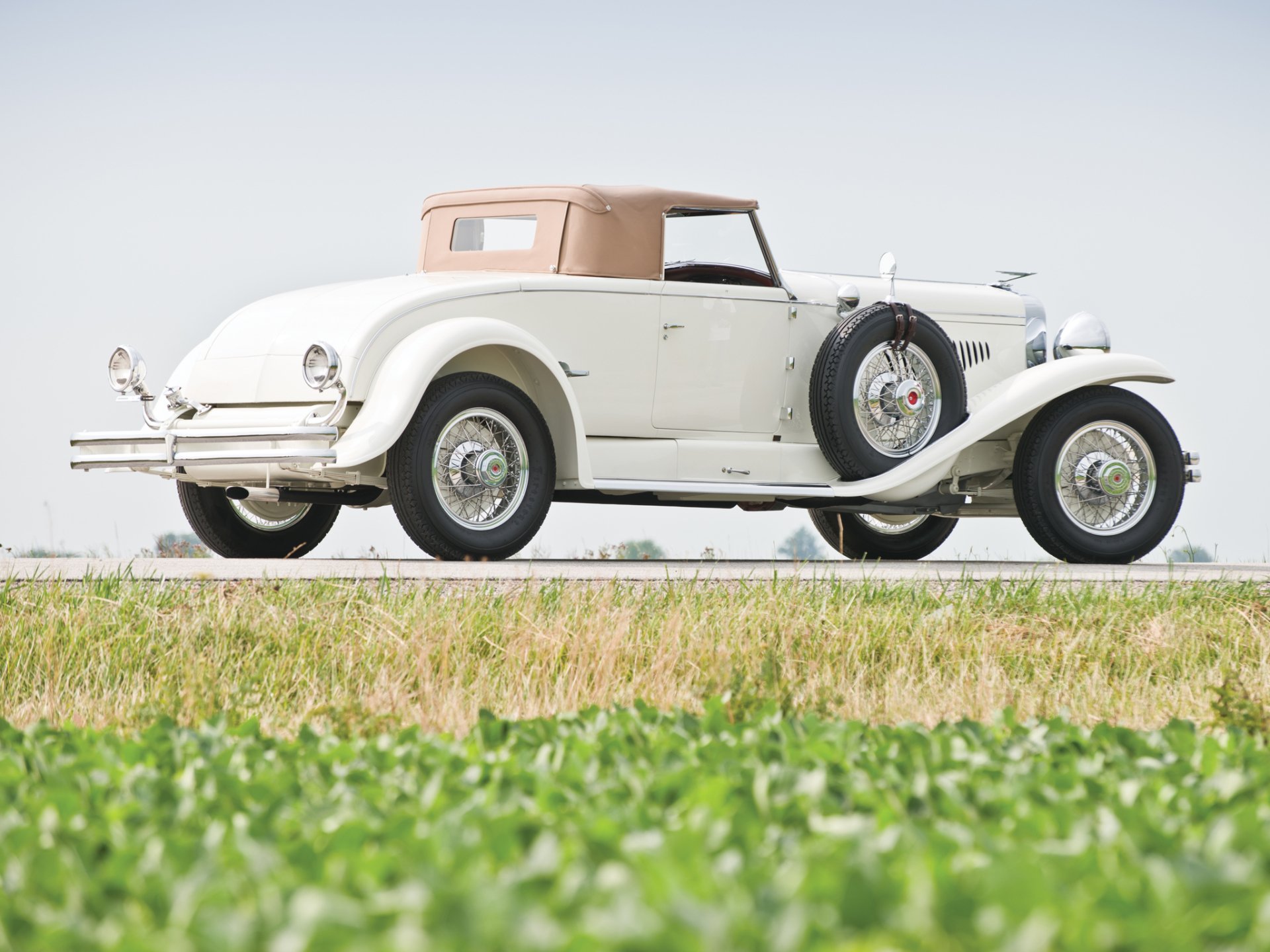 Vintage 1929 Duesenberg Model J Convertible Coupe in white, showcased as a classic vehicle against a clear sky and green field, captured in HD for a desktop wallpaper.
