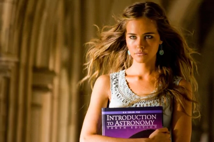 Blonde woman with green eyes holds an Introduction to Astronomy book in a scene from Transformers: Revenge of the Fallen. HD wallpaper with a cinematic feel.