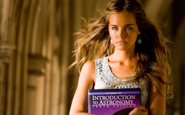 Blonde woman with green eyes holds an Introduction to Astronomy book in a scene from Transformers: Revenge of the Fallen. HD wallpaper with a cinematic feel.
