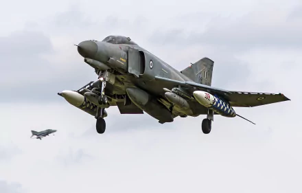 McDonnell Douglas F-4 Phantom II jet fighter warplane in military colors landing against a cloudy sky with a second F-4 in the distance — 2K Quad HD PC desktop wallpaper background.