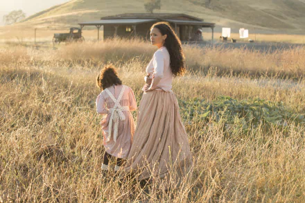 A serene moment from the TV show Westworld featuring Thandie Newton and a child, Jasmyn Rae, walking through a golden grassy field, captured in a stunning HD wallpaper.